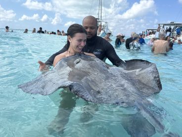 A joyful interaction as a woman swims with a stingray, guided by an instructor in crystal-clear waters — a memorable wildlife experience in the Bahamas.