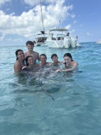 A group of six people joyfully interacts with a stingray in shallow waters, creating a memorable wildlife experience in a tropical paradise.