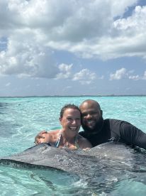 A joyful encounter as two individuals interact closely with a stingray in the clear waters, showcasing a unique wildlife experience in a tropical paradise.
