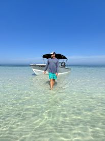 A man walks through shallow waters towards a boat, capturing the essence of a perfect beach day. Ideal for showcasing water activities and relaxation.