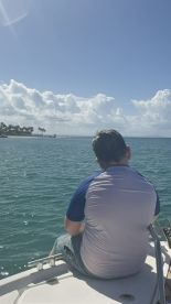 A person enjoys a serene moment on the edge of a boat, overlooking the tranquil ocean and picturesque clouds — a perfect setting for relaxation and adventure on the water.