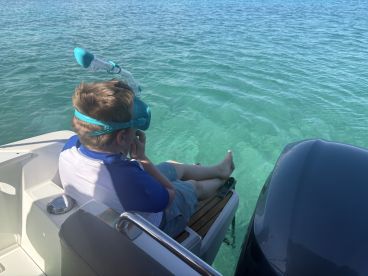A child prepares to snorkel while sitting on the edge of a boat, enjoying the clear turquoise waters — a perfect moment for family adventures on the water.