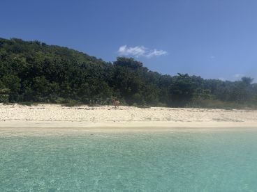 A serene view of a beach with clear turquoise waters and a person exploring the shoreline, perfect for showcasing tropical island getaways.