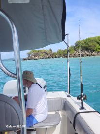 A man relaxes on a boat while enjoying the scenic view of an island, with snorkelers visible in the turquoise waters — perfect for a day of fishing and exploration.