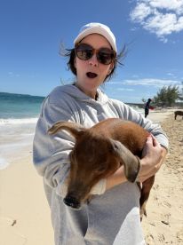 A woman joyfully holds a pig on the beach, showcasing a unique and playful interaction with wildlife — a memorable experience in the Bahamas.
