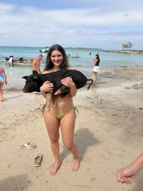 A young girl joyfully holds a pig while enjoying a beach day, showcasing a unique wildlife interaction in the Bahamas.