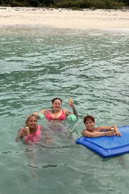 A joyful group enjoys a refreshing swim in crystal-clear waters, sipping cocktails and soaking up the sun — a perfect beach day experience.