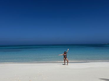 A joyful moment captured on a pristine beach, with a woman celebrating under the clear blue sky and turquoise waters — a perfect snapshot of a tropical getaway.
