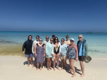 A cheerful group poses on the beach, enjoying a sunny day by the turquoise waters — perfect for family gatherings or beach celebrations.