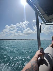 A guest enjoys a refreshing drink while soaking up the sun on a boat, with beautiful turquoise waters and a scenic backdrop — perfect for a day of fun on the water.