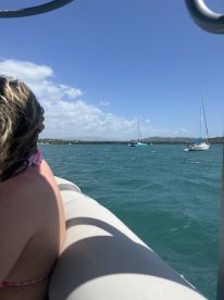A scenic view from a boat with a passenger enjoying the ride, showcasing other sailboats in the distance — perfect for a day of sailing and relaxation on the water.