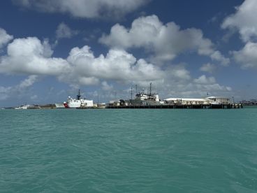 A scenic view of a U.S. Coast Guard vessel docked at a harbor, surrounded by turquoise waters and a backdrop of fluffy clouds.