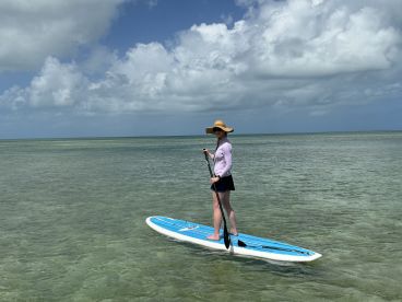 A woman enjoys paddleboarding in clear waters under a beautiful sky, showcasing the perfect outdoor adventure on the water.