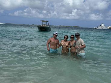 A group of friends enjoys a fun day at the beach, celebrating with cocktails in the shallow water while a boat is anchored nearby.