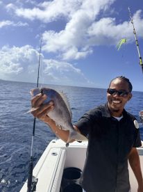 A proud angler holds up a freshly caught fish while fishing in the open ocean, showcasing the thrill of deep-sea fishing adventures.