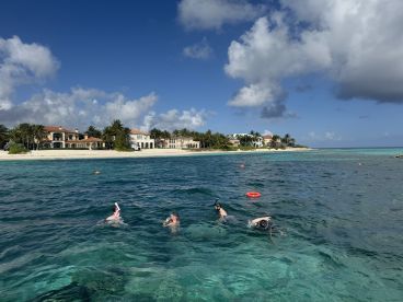 A group enjoys snorkeling in the clear waters near a beautiful beach, with stunning coastal homes in the background — a perfect tropical getaway experience.