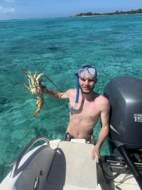 A snorkeler proudly displays a freshly caught lobster in the stunning turquoise waters, showcasing the excitement of underwater adventures.