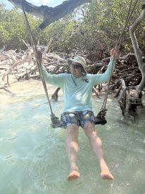 A man enjoys swinging over shallow waters surrounded by mangroves, capturing a moment of relaxation and fun in nature.