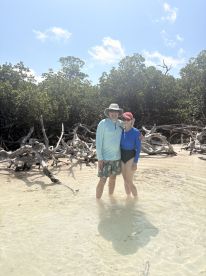 A couple enjoys a sunny day wading in shallow waters surrounded by mangroves, capturing the essence of a tropical beach adventure.