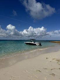 A sleek speedboat is docked on a pristine beach, surrounded by clear turquoise waters and a vibrant sky, perfect for a day of relaxation and adventure.