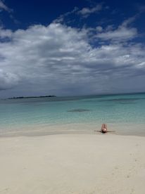 A serene beach scene featuring a person relaxing on the shore, surrounded by crystal-clear waters and a beautiful sky — an ideal getaway for sunbathing and tranquility.