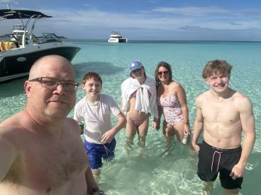 A joyful family enjoys a sunny day at the beach, wading in clear waters with their pontoon boat in the background — perfect for summer adventures and family bonding.