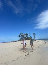 Two friends explore a beautiful beach on a secluded island, surrounded by palm trees and clear blue skies — a perfect setting for adventure and relaxation.