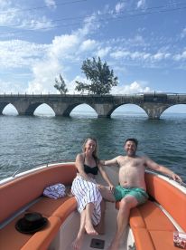 A couple enjoys a sunny day on a boat, relaxing with a scenic bridge in the background — perfect for romantic getaways or leisurely outings on the water.