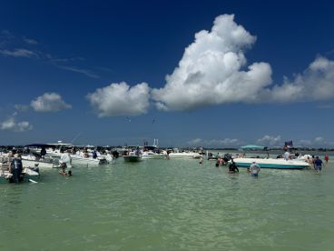 A lively scene at a sandbar with numerous boats and people enjoying the water, making it a perfect spot for summer fun and social gatherings.