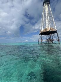An unclear view of a lighthouse structure over turquoise waters, with no identifiable subjects or activities.