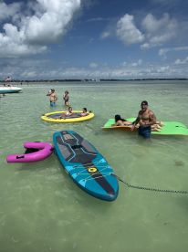 A lively group enjoys a day at the beach, swimming and paddleboarding in shallow waters — perfect for family fun and relaxation.