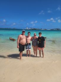 A joyful family poses together on a beautiful beach, enjoying their time in the sun with clear turquoise waters in the background — a perfect snapshot of island fun.