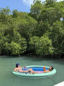 A couple enjoys a relaxing day on a floating mat in serene mangrove waters, perfect for unwinding and soaking up the sun.
