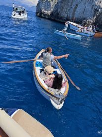 A group enjoys a scenic boating experience on the ocean, with one person pointing out sights while others relax in a small rowboat.