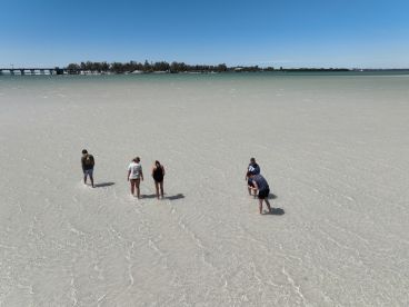 A group of friends enjoys a fun day at the beach, wading in shallow waters — a perfect sandbar stop for relaxation and exploration.