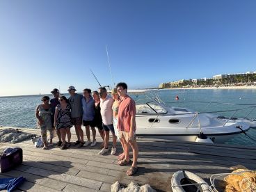 A cheerful group poses for a photo on the dock next to a boat, capturing a memorable moment by the beach — perfect for family gatherings or vacation celebrations.