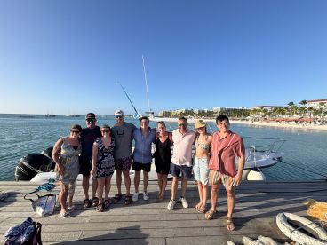 A cheerful group poses together on the dock with a boat in the background, capturing a memorable moment by the beach — perfect for family gatherings or vacation celebrations.