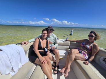 A lively group enjoys a sunny day on a pontoon boat, relaxing and sipping drinks while surrounded by clear waters — perfect for a fun day out on the water.