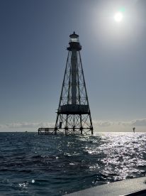 A lighthouse stands tall against a bright sky, surrounded by shimmering waters, capturing a serene maritime scene.