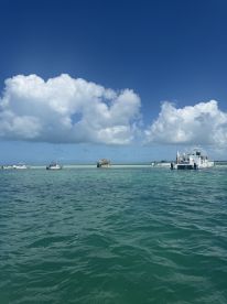 A picturesque view of several boats anchored near a sandbar, showcasing the beautiful turquoise waters and clear blue skies — an ideal setting for a day of relaxation and fun on the water.