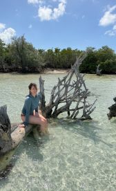 A young woman enjoys a serene moment sitting on a mangrove in shallow waters, surrounded by lush greenery — a perfect snapshot of a tropical getaway.