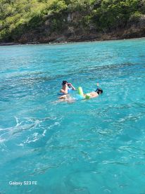 Two individuals enjoy snorkeling in the crystal-clear waters, surrounded by stunning natural scenery — a perfect day for aquatic adventures.