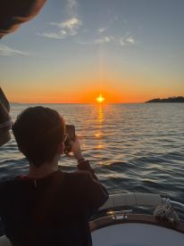 A child captures the stunning sunset from the deck of a boat, creating a picturesque moment perfect for family outings on the water.