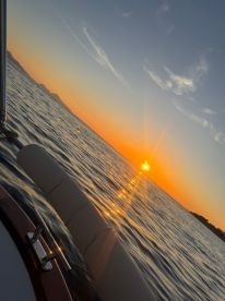 A serene sunset view from the deck of a boat, showcasing the tranquil waters and distant land — perfect for romantic evening cruises.