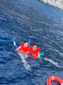 A joyful couple enjoys snorkeling in crystal-clear waters, wearing life jackets for safety — a perfect adventure for water lovers.