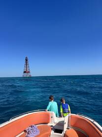 Two children enjoy the view from a boat, overlooking a lighthouse and snorkelers in the vibrant blue ocean — a perfect family adventure on the water.
