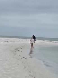 A couple enjoys a serene walk along the beach, capturing the tranquil beauty of the shoreline on a cloudy day.