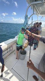 A young boy proudly holds up his catch while fishing on a boat, surrounded by family enjoying a fun day on the water.
