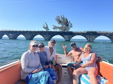 A cheerful group of friends enjoys a day on the water, posing on their boat with a scenic bridge in the background — perfect for memorable outings and adventures.