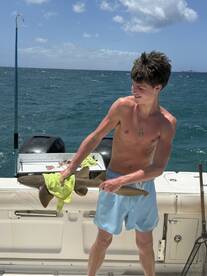 A young boy proudly holds a shark he caught while fishing on a boat, showcasing an exciting wildlife encounter on the water.